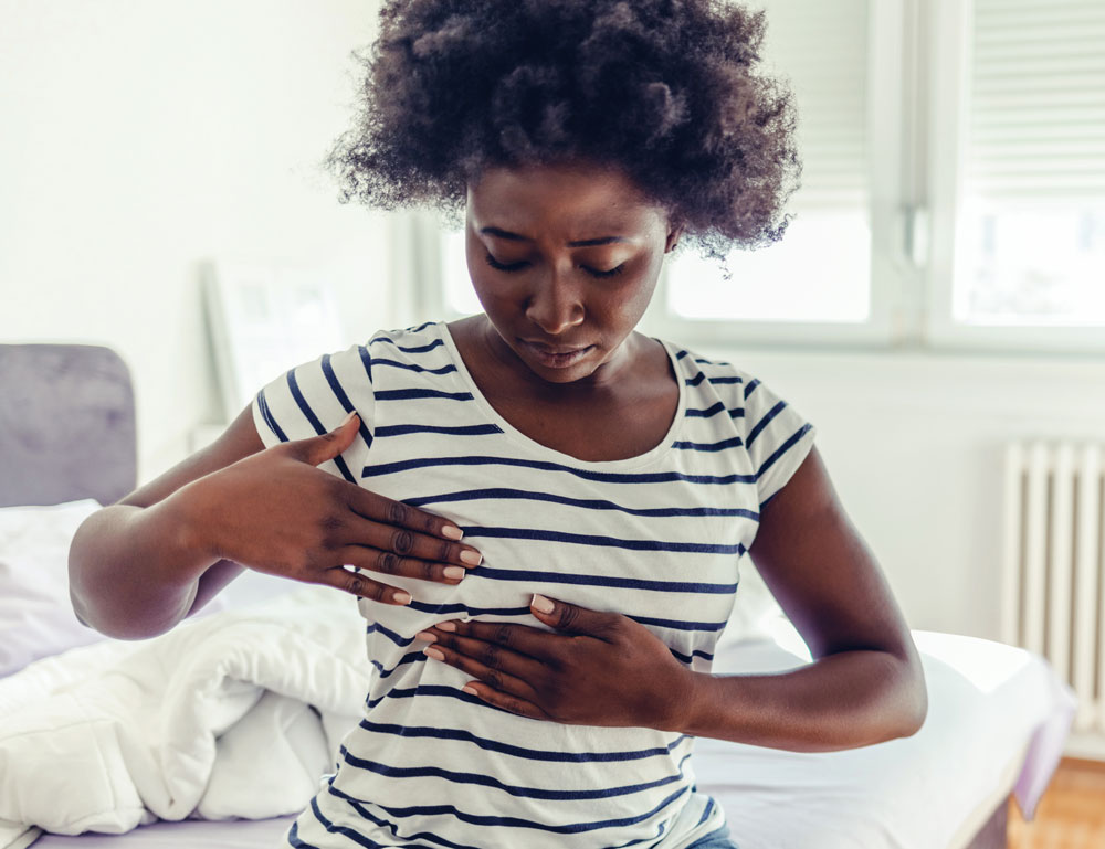 Woman examining her breast while sitting on a bed